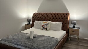 Ein Schlafzimmer mit einem gesteppten Kopfteil, einem Bett mit grauer Bettdecke, zwei Nachttischen mit Lampen und einer Klimaanlage an der Wand.