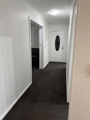 Un pasillo con paredes blancas y alfombra oscura, que conduce a una puerta con un panel de vidrio decorativo.