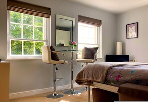 Ein Schlafzimmer mit einem Bett, zwei Stühlen, einem Schreibtisch, einem Spiegel und einem Fenster mit Blick auf Bäume.