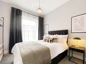 A modern bedroom with a large bed, a bedside table, a lamp, and a window with curtains. - Spacious 3BR Home in Walkden Garden Parking (Moffat)