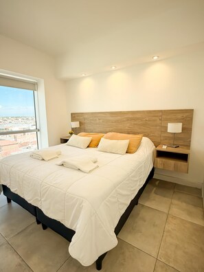 Un dormitorio con una cama grande, dos mesitas de noche, un cabecero de madera y una ventana con vistas a la ciudad.