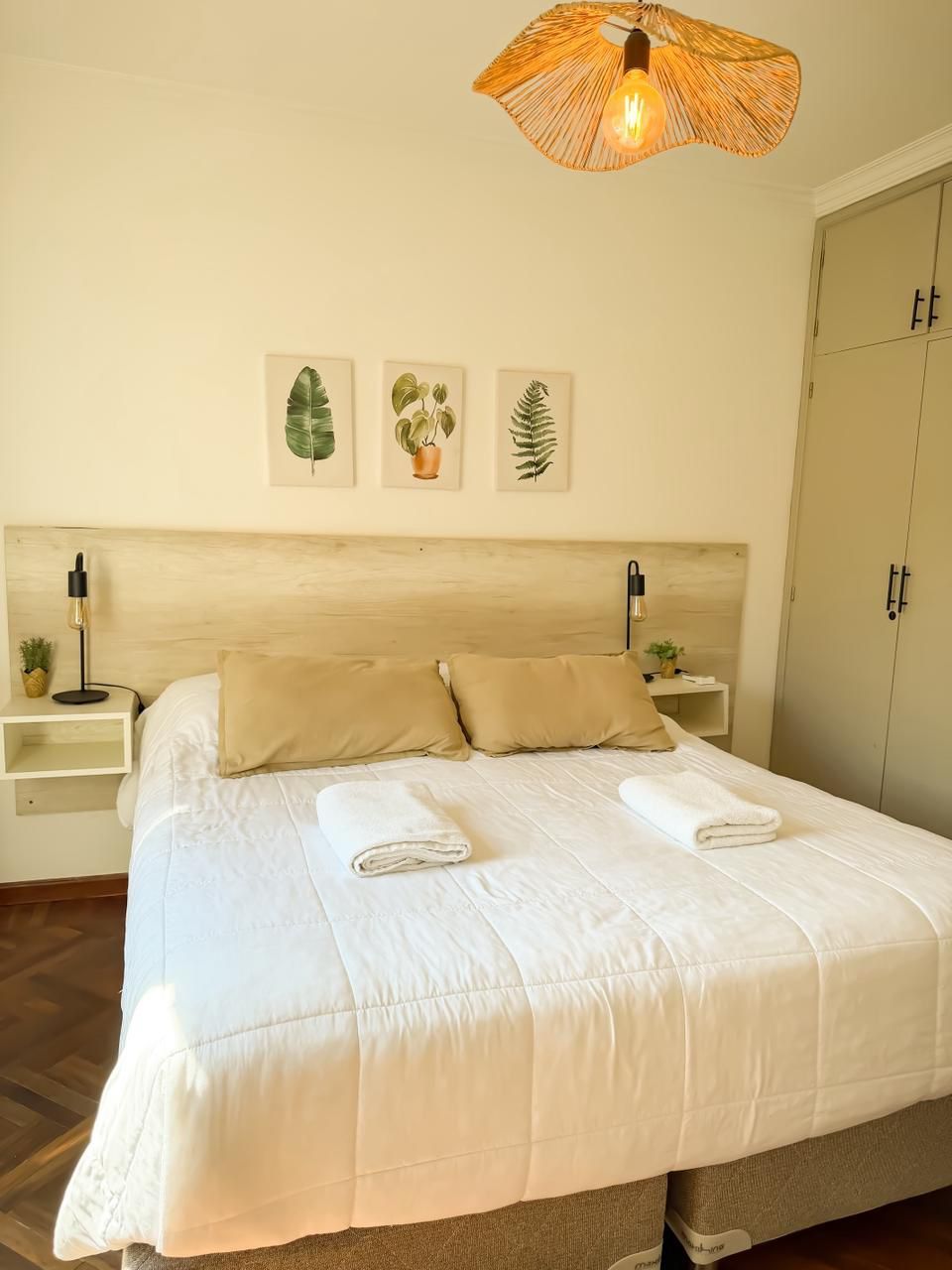 A neatly made bed with white linens and two pillows, a bedside table with a lamp, and a wall-mounted light fixture.