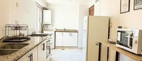 Cocina con armarios blancos, encimera de granito, microondas, cubo de basura y pileta.