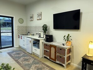A compact kitchen with a refrigerator, microwave, coffee maker, and a TV mounted on the wall.