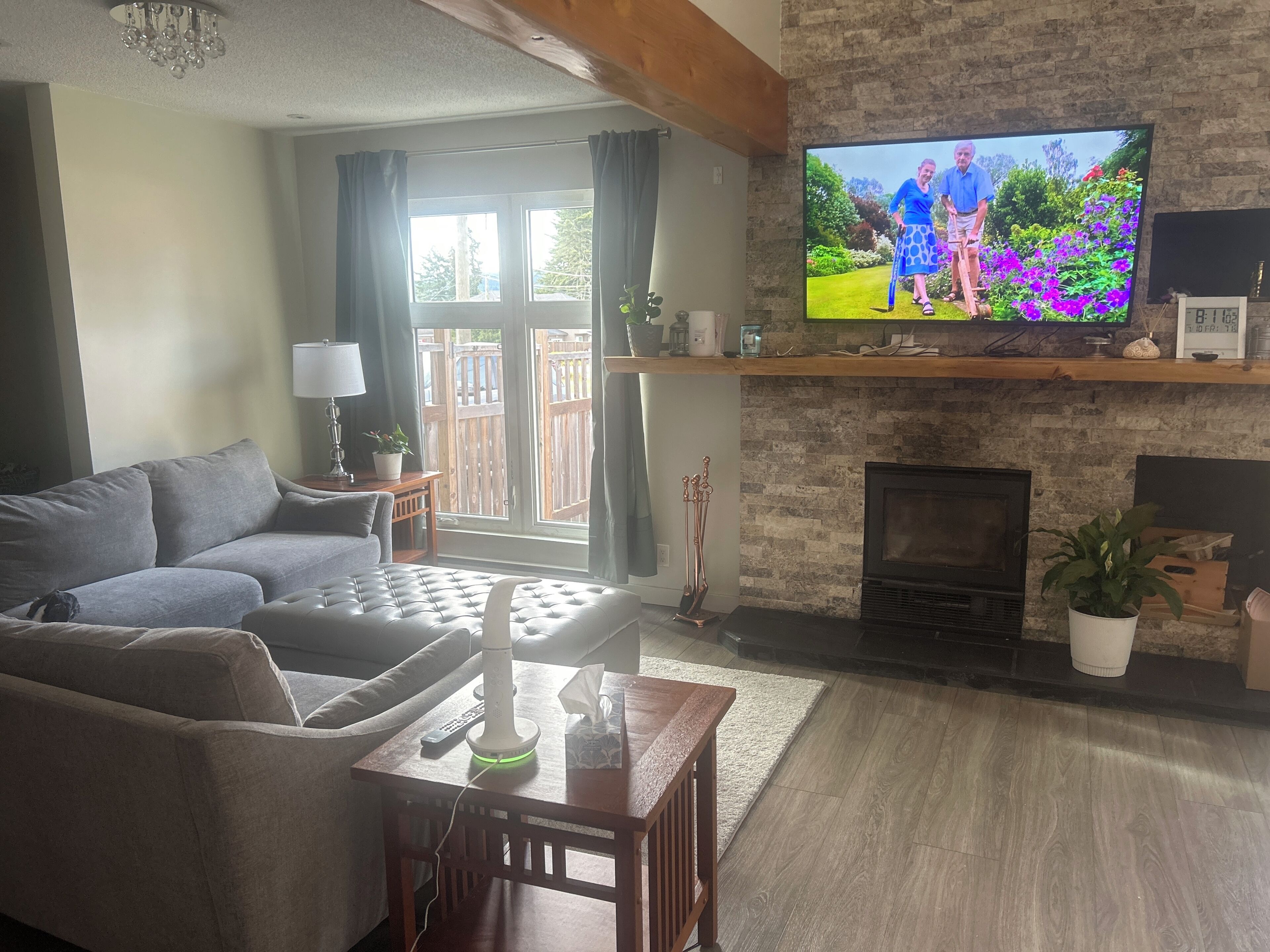 A living room with a sofa, a table with a lamp, a fireplace, and a television displaying a garden scene.