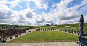 Ein grünes Feld mit einer Steinsäule, einer Statue und zwei Gebäuden in der Ferne.