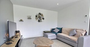 Ein modernes Wohnzimmer mit Flachbildfernseher, Couchtisch aus Holz, grauem Sofa und einer dekorativen Wandarbeit.