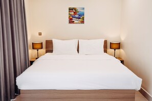 Una cama bien hecha con sábanas blancas, dos l ámparas de noche y un cuadro sobre la cama.