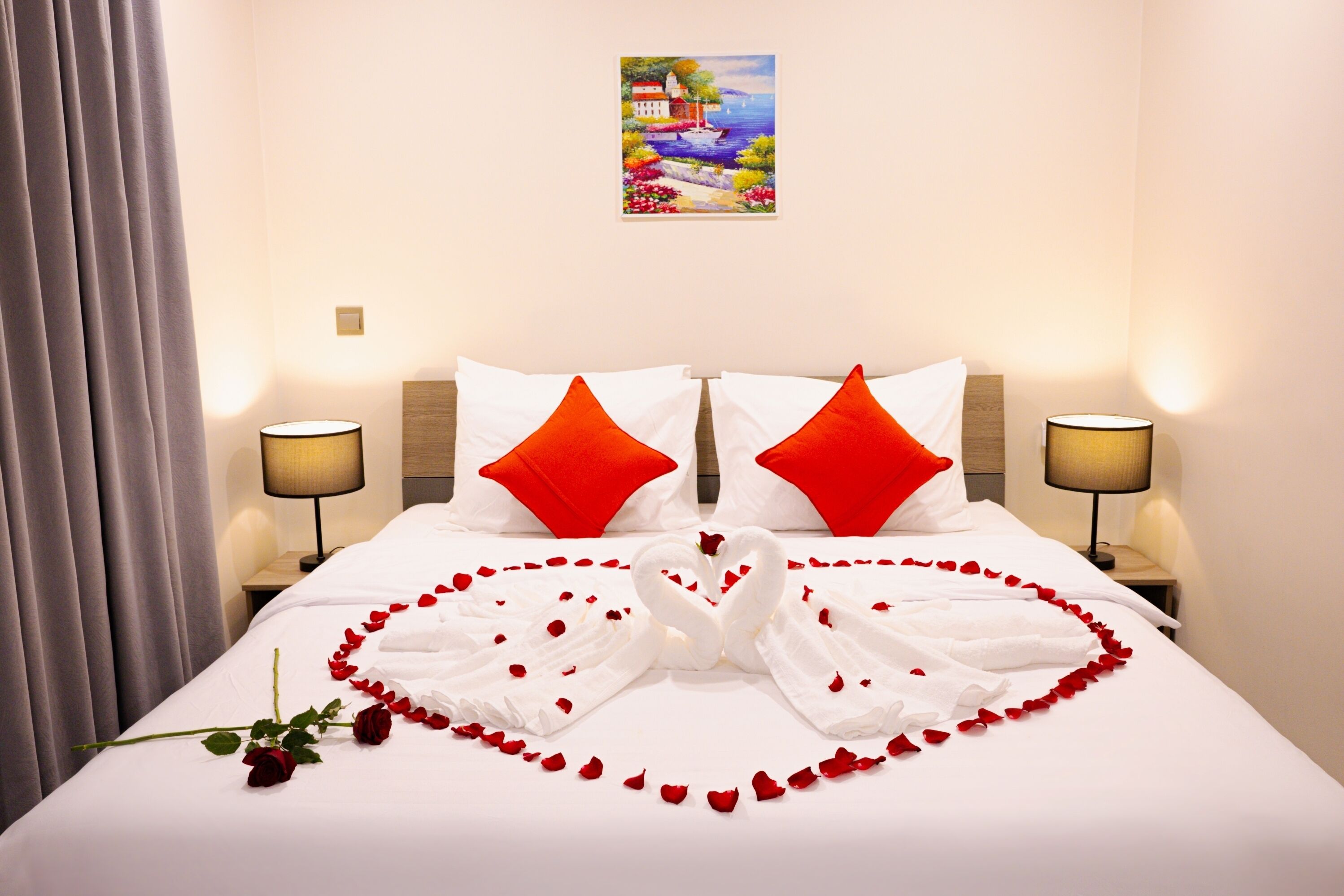 Una camera d'albergo con un letto, due cuscini rossi, un quadro appeso e un bouquet di rose.