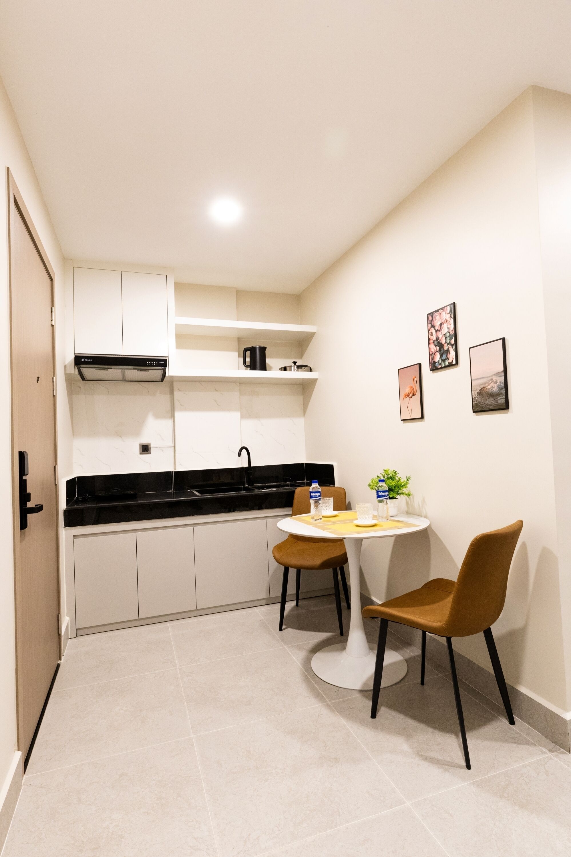 A compact kitchen with white cabinets, a black countertop, and a small dining table with two chairs.