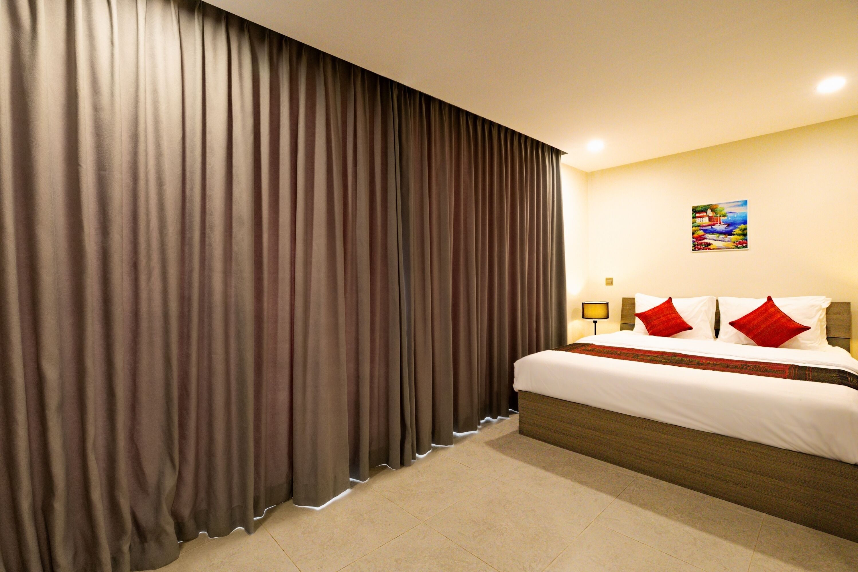Een hotelkamer met een groot bed, gordijnen, een bedlampje en een schilderij aan de muur.