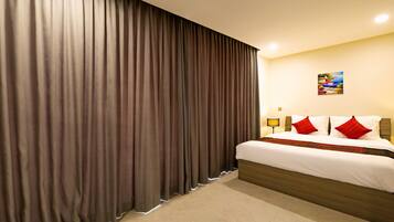 Een hotelkamer met een groot bed, gordijnen, een bedlampje en een schilderij aan de muur.