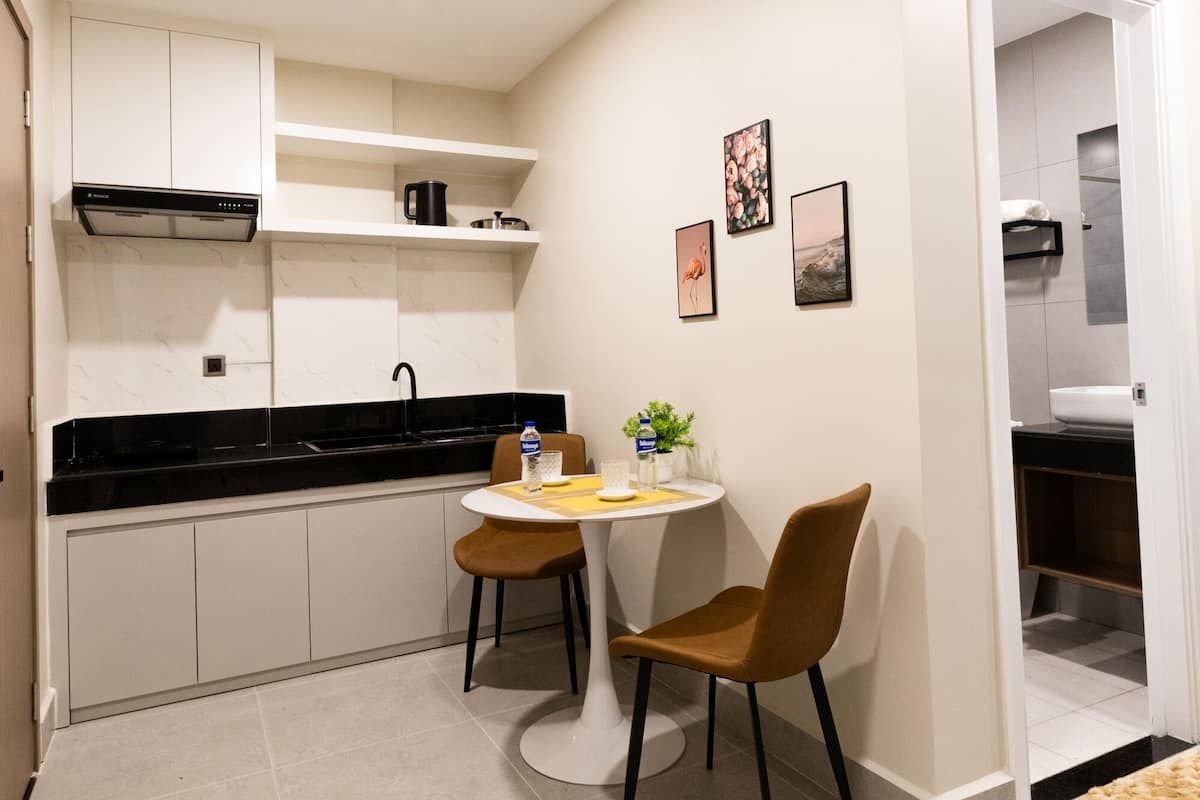 Una cocina compacta con comedor, muebles de cocina blancos, encimera negra y una pequeña mesa con sillas.