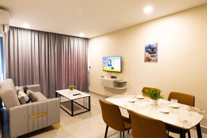 A modern living room with a sofa, a dining table with chairs, a flat-screen TV, and a potted plant.