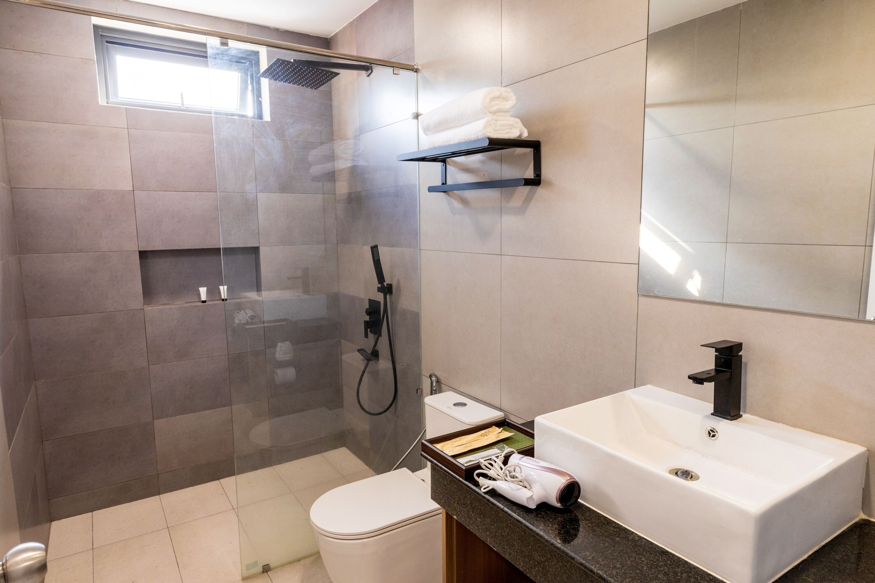 Un baño moderno con ducha envuelta en vidrio, un lavamanos blanco y un inodoro.