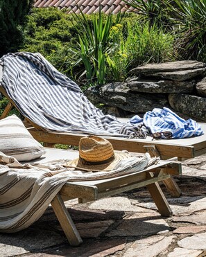 Two wooden lounge chairs with striped towels and a straw hat, set on a stone patio with greenery in the background. - Historic house in southern France (Mons La Trivalle)