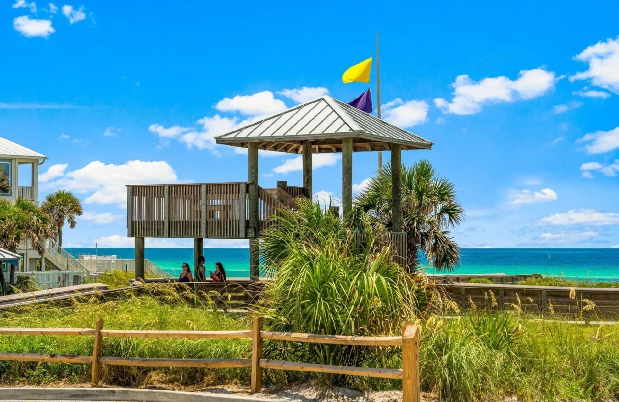 A beach gazebo with a flag, palm trees, and a view of the ocean.
