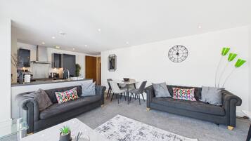 Ein modernes Wohnzimmer mit zwei Sofas, einem Esstisch und einer Küche im Hintergrund.