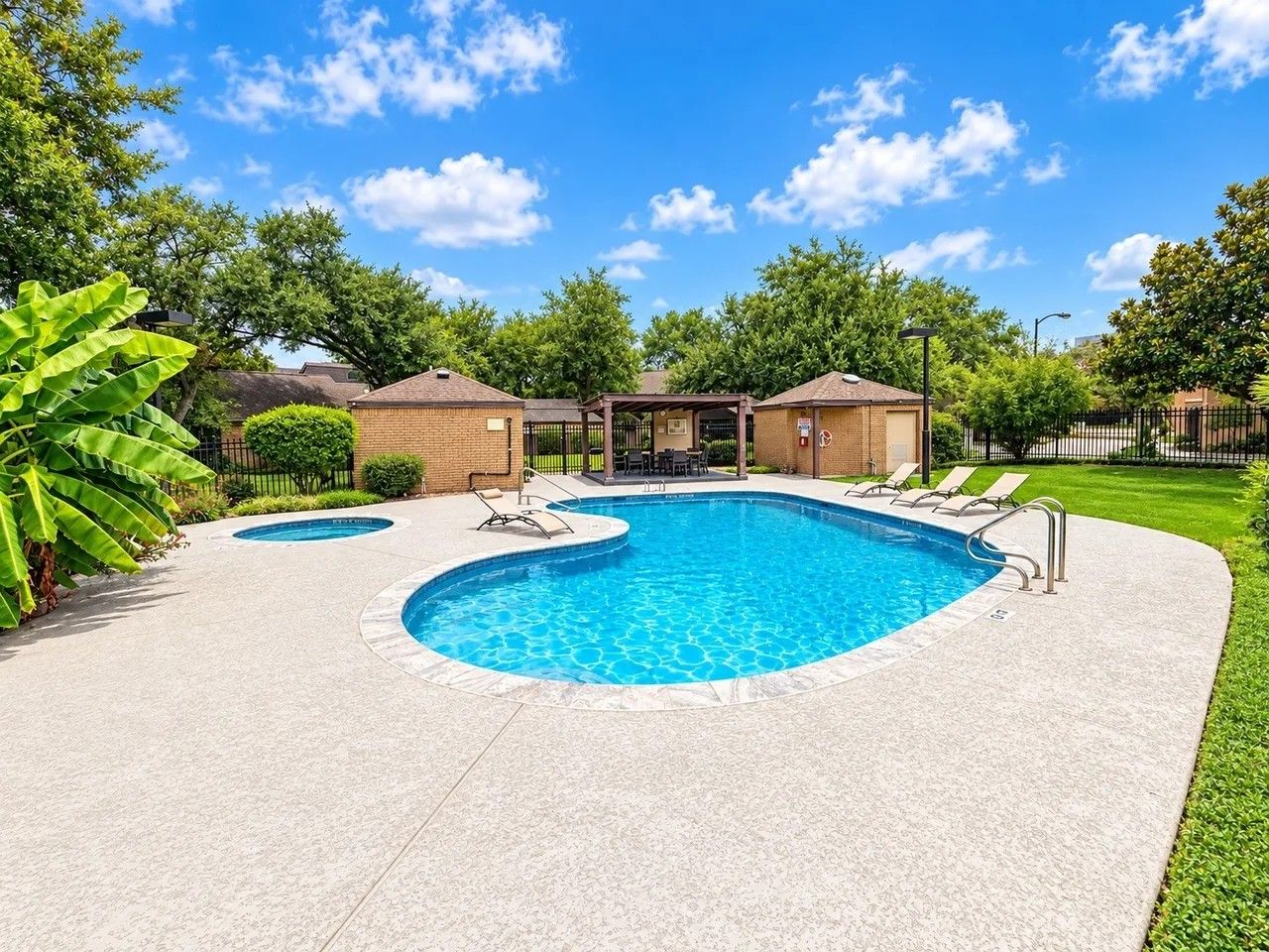A rectangular swimming pool with a surrounding deck, two lounge chairs, and a covered seating area.