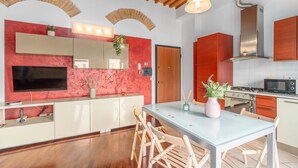 Una cocina moderna con televisor, armarios de madera, una mesa de comedor con sillas y una pared de acento roja.