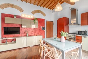 Une cuisine moderne équipée d’un téléviseur, de meubles en bois, d’une table à manger avec des chaises et d’un mur d’accent rouge.