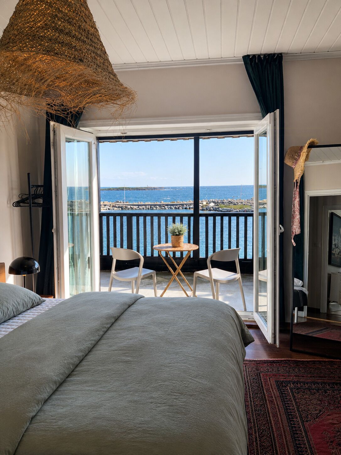 A bedroom with a large bed, a small table with chairs, a view of the sea, and a fireplace.