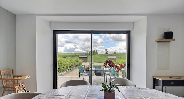 Ein Zimmer mit einer großen SchiebeglasTür, die auf eine Terrasse mit Tisch und Stühlen, einem Blumentopf und einem kleinen Holzregal führt.
