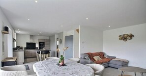 Ein modernes Wohnzimmer mit Esstisch, Sofa und einer Küche im Hintergrund.