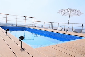 Ein Pool auf dem Dach mit freiem Blick auf die Stadtlandschaft, eine Holzterrasse und eine Lounge-Bereich mit einem gestreiften Sonnenschirm.