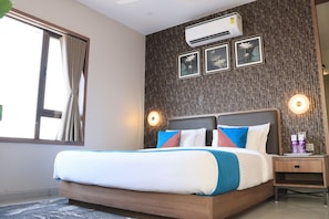Quarto de hotel com cama, ar condicionado, luminárias fixadas na parede e obra de arte emoldurada.