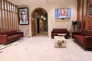 A lobby with two red sofas, a marble coffee table, a TV, and a framed artwork on the wall. - Pride Elite, Dwarka (Dwarka)