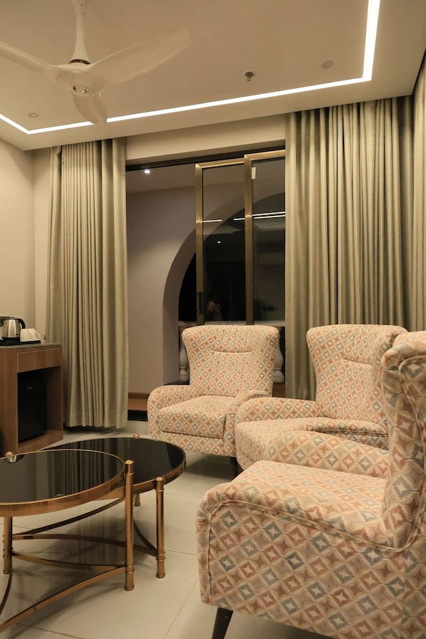 Uma sala de estar moderna com um ventilador de teto, uma mesa de centro de vidro, poltronas estampadas e uma TV sobre um suporte de madeira.