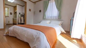 Un dormitorio con cama, ventana con cortinas, kitchenette y baño.