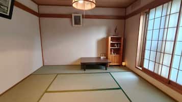 Tatami-mattoilla päällystetty huone, jossa on matala pöytä, riippuvalaisin, puinen kaappi ja ikkuna, jossa on shoji-paperiset ikkunanpuitteet.