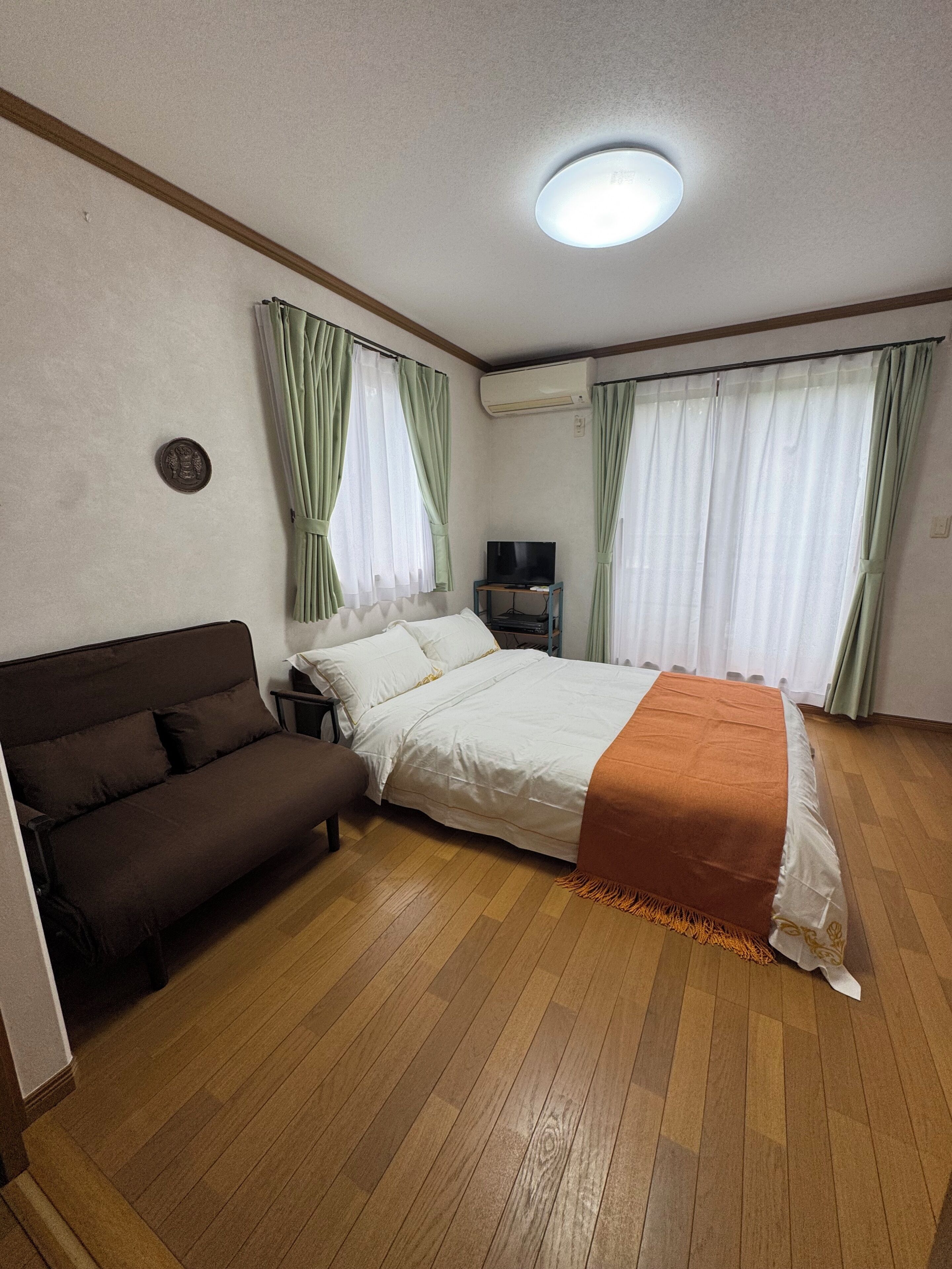 A bedroom with a bed, a sofa, a TV, and an air conditioning unit.
