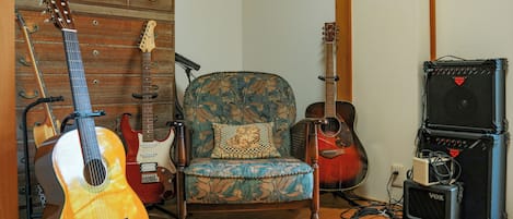 A room with a wooden wall, a patterned armchair, and various musical instruments including guitars and amplifiers.