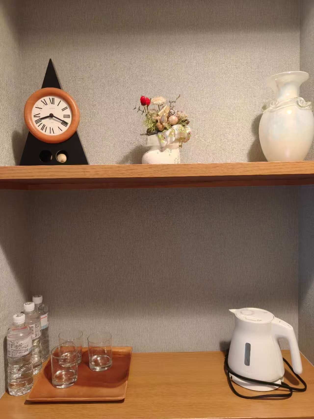 Une étagère avec une horloge, un vase de fleurs, une carafe et une bouilloire, le tout posé sur une table.