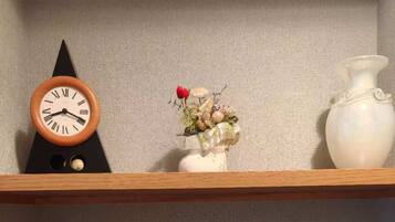 Une étagère avec une horloge, un vase de fleurs, une carafe et une bouilloire, le tout posé sur une table.
