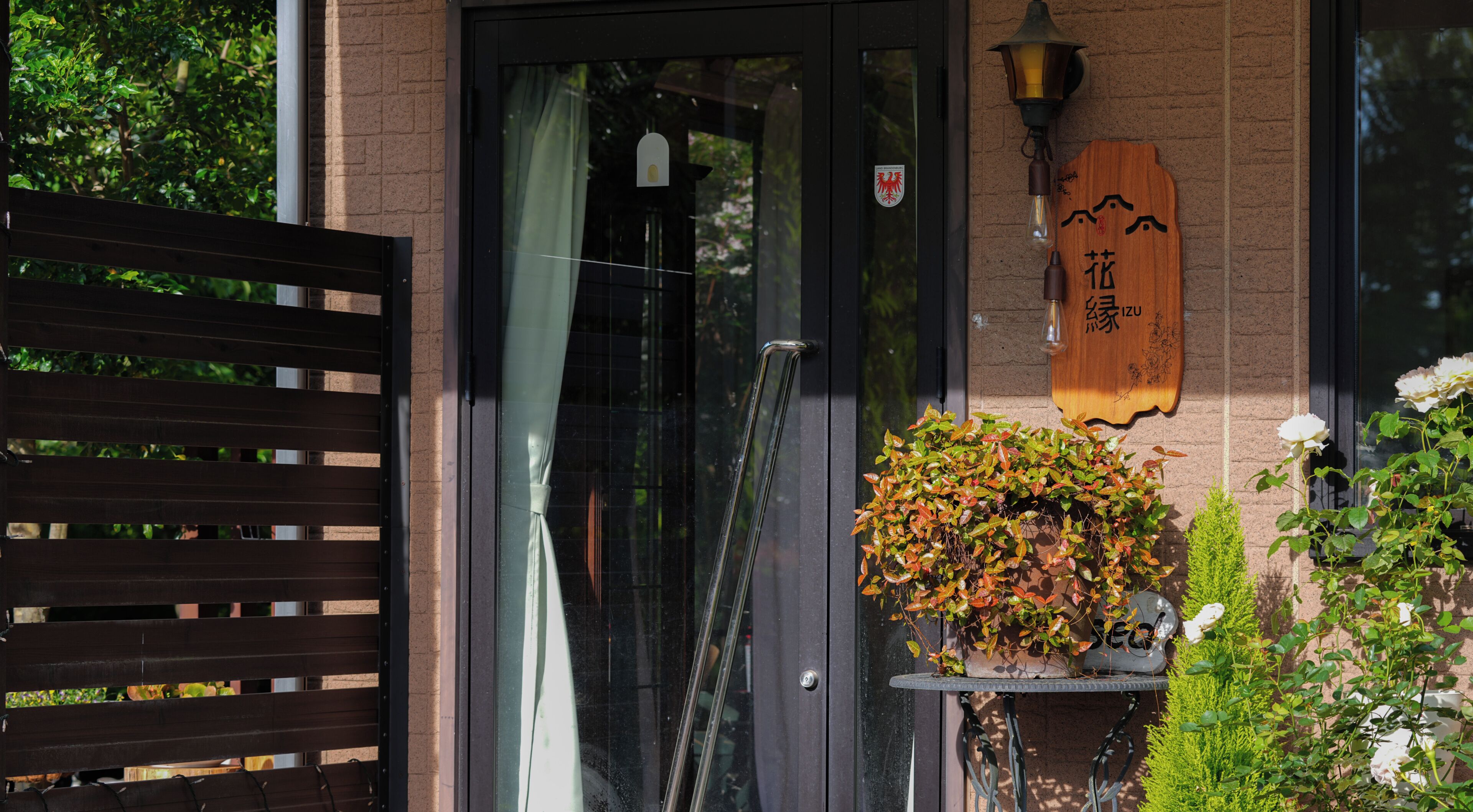 A wooden sign with characters, a glass door, a metal gate, and a potted plant with foliage.