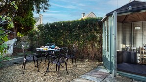 Un patio con tavolo e sedie, circondato da un siepe e un muro in pietra.