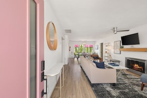 A modern living room with a fireplace, a TV mounted on the wall, and a dining area in the background. - Desert Divas Escape - Palm Springs (Palm Springs)
