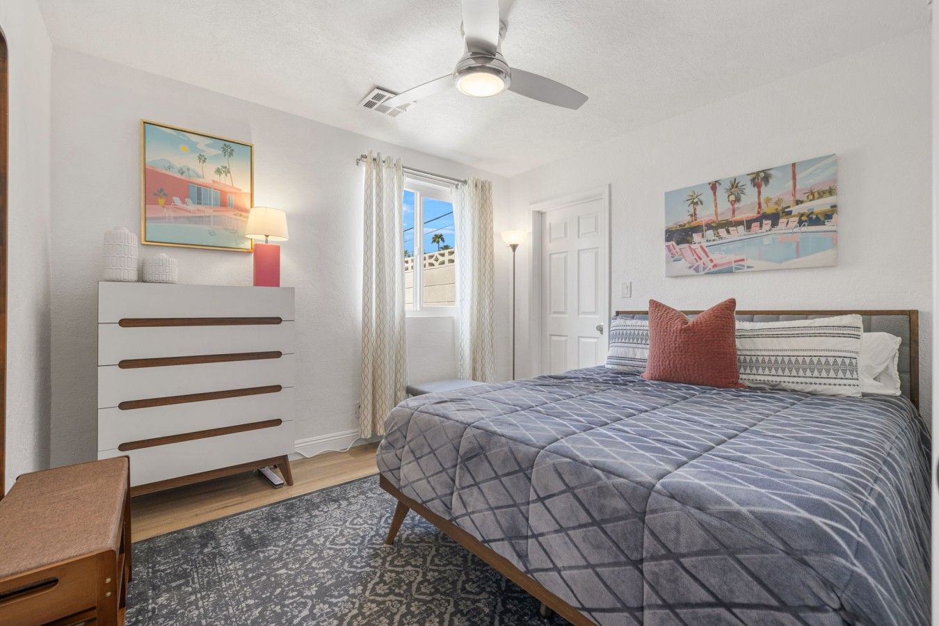 A bedroom with a bed, a dresser, a ceiling fan, and two paintings on the walls.