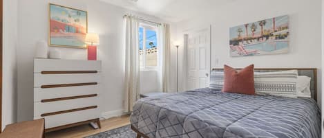 A bedroom with a bed, a dresser, a ceiling fan, and two paintings on the walls.