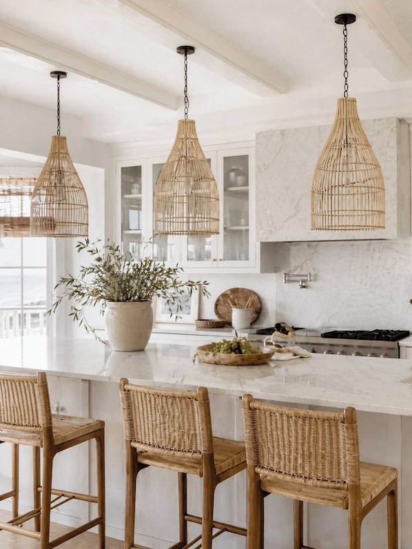 A kitchen with a central island, three wicker pendant lights, and a potted plant. - Lakefront on Chesapeake in North Dewey (Dewey Beach)