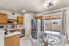 A modern kitchen with wooden cabinets, stainless steel appliances, a glass dining table, and a sliding glass door to the outside.