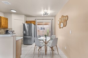 A modern kitchen with a stainless steel refrigerator, wooden cabinets, a glass dining table with four chairs, and a sliding glass door leading to a balcony.