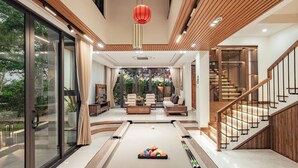 A modern living room with a pool table, a staircase, and a view of a garden. - Hometown Kem 4 BRS Pool Villa Hoi An (Hoi An)