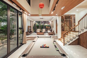 Ein modernes Wohnzimmer mit Billardtisch, einer Treppe und Blick auf einen Garten.