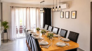 Un coin repas avec une longue table dressée pour six personnes, des chaises noires et une plante en pot.