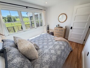 Une chambre à coucher avec un grand lit, une commode, un miroir et une vue sur un paysage verdoyant par la fenêtre.